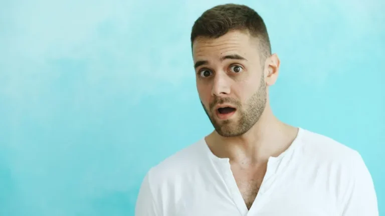 Surprised man in a white t-shirt against a blue wall