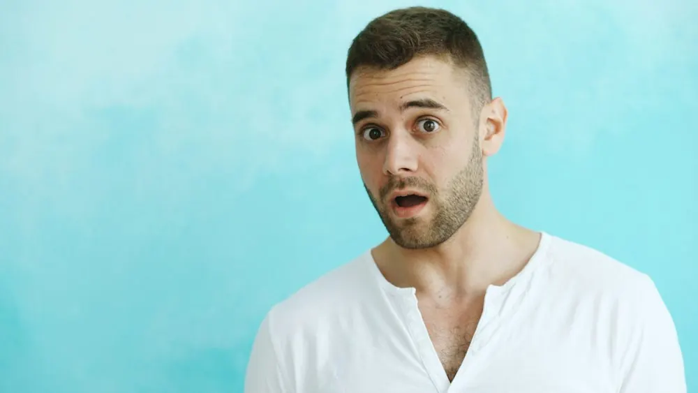 Surprised man in a white t-shirt against a blue wall