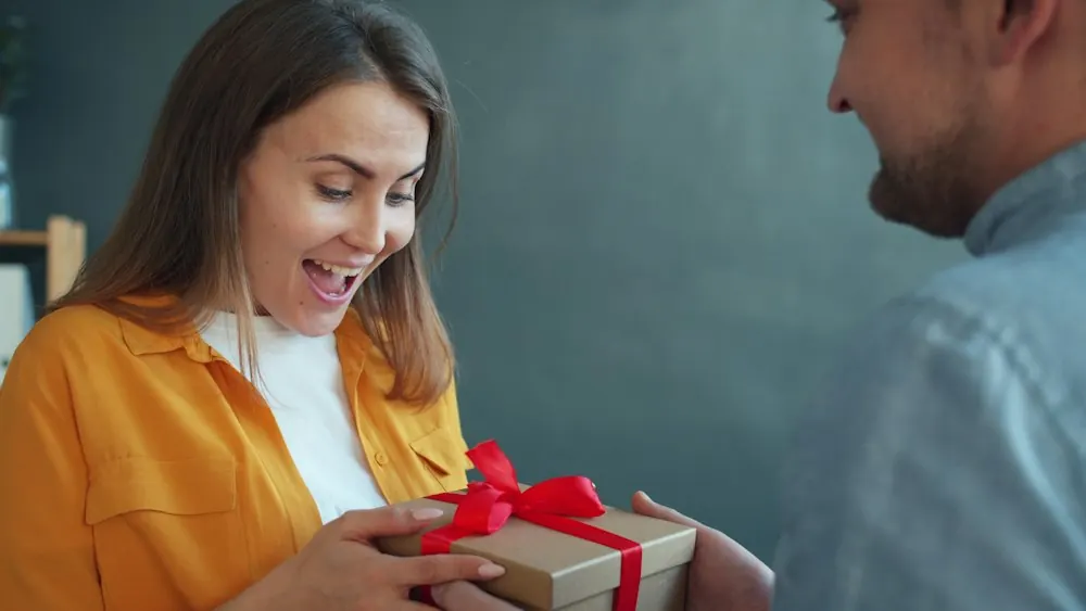 Woman smiling as she is handed a wrapped gift with a red ribbon